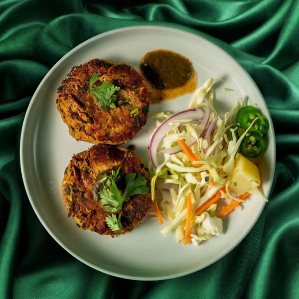 Two golden-brown patties with cilantro, a side salad, and sauce on a white plate.