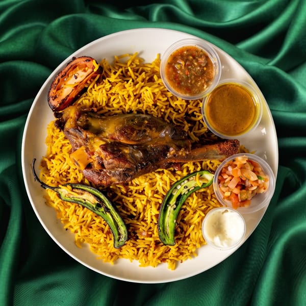 Mandi rice with lamb shank, grilled vegetables, and three dipping sauces on a green silk background.