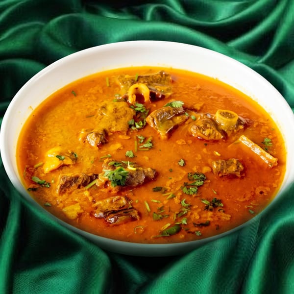 A white bowl of rich orange curry with meat and cilantro sits on a draped green fabric.