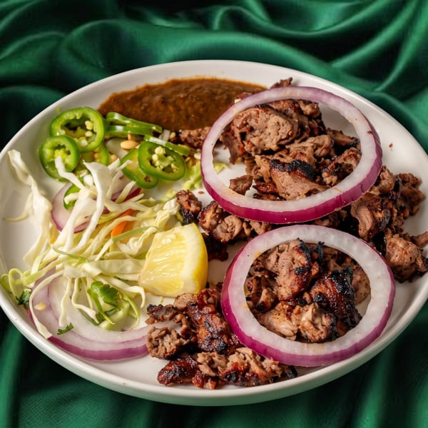Grilled meat with red onion, shredded cabbage, jalapeños, and a lemon wedge on a white plate.