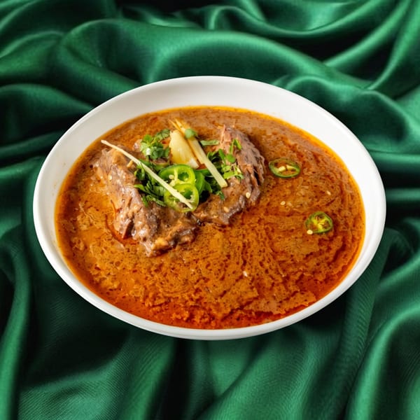 A bowl of haleem, a stew of meat and lentils, garnished with ginger, cilantro, and green chilies.